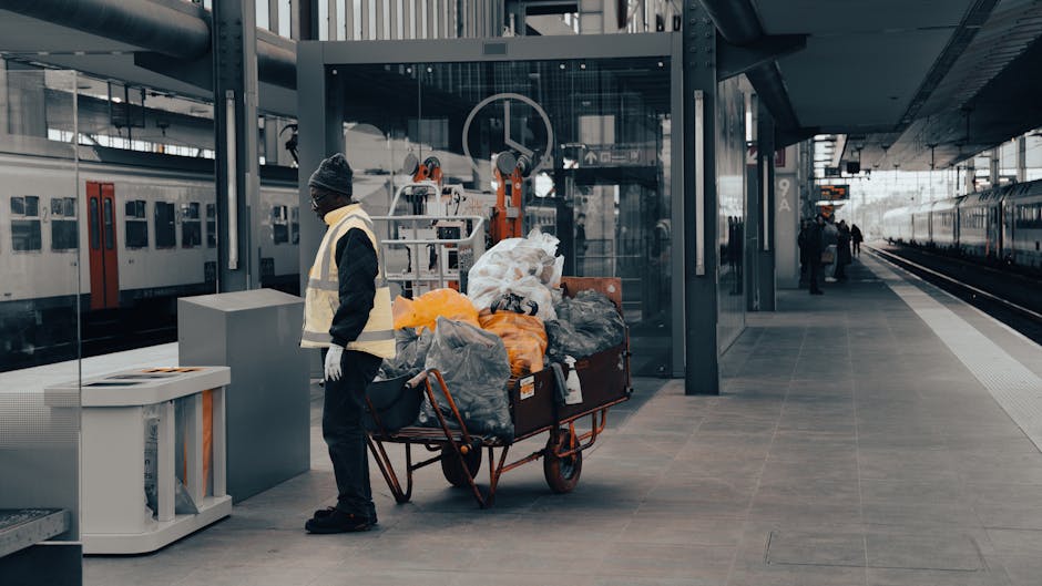 A collection of overflowing waste bins and scattered rubbish bags on a paved sidewalk outside a commercial area, with various types of waste including cardboard boxes, plastic bags, paper, and packagi